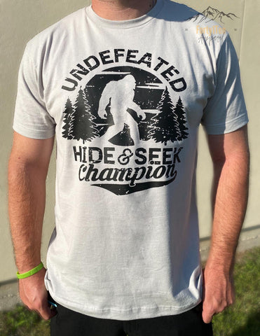 Silver Tee with Distressed Black " Undefeated Hide & Seek Champion " Design.